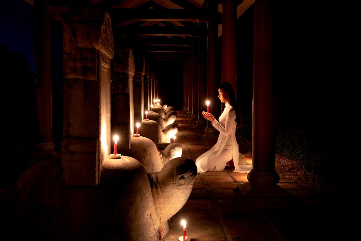 A serene image of a woman kneeling and praying in a temple illuminated by candlelight.
