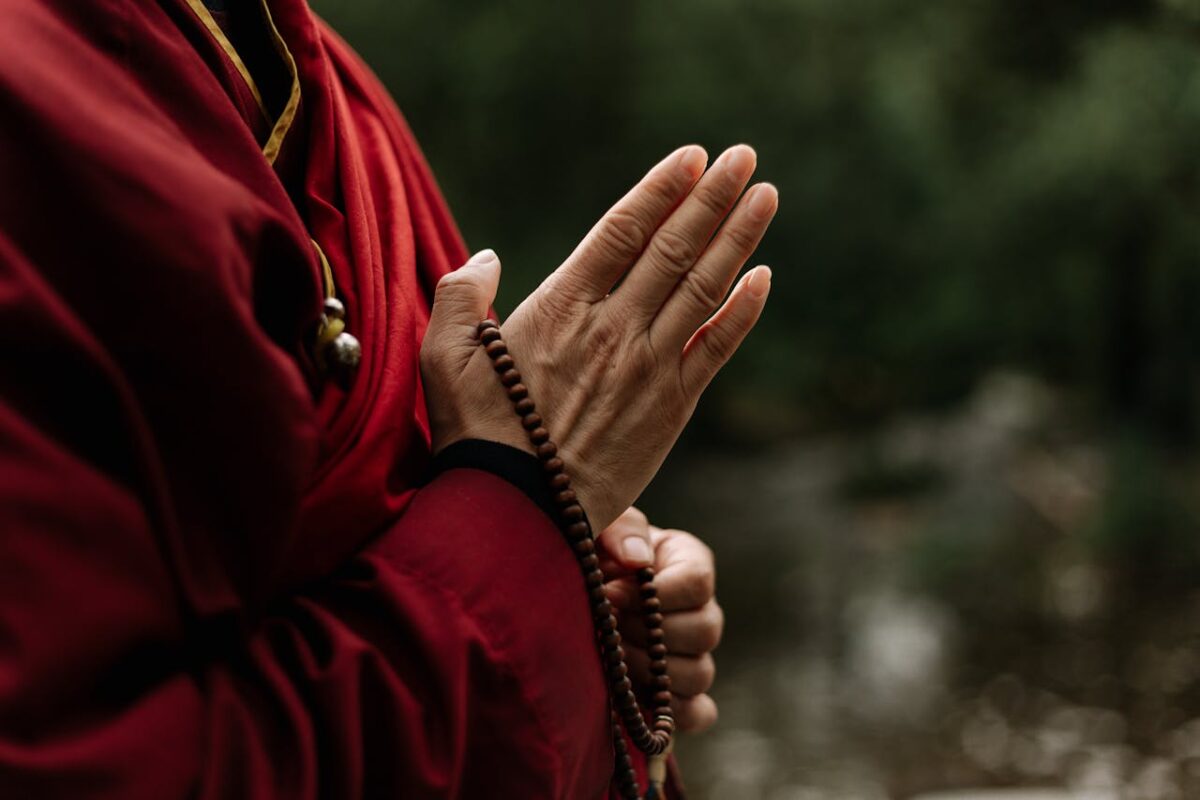Close-up of monk in red robe meditating with prayer beads outdoors.